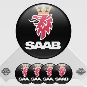 May include: Black round button featuring the Saab logo: a red griffin with a gold crown, and the word "SAAB" in white. The image shows a large button and four smaller buttons with the same design.