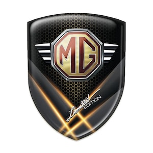 Op de afbeelding: Een glanzend zwart en goud schildvormig embleem met de letters "MG" in een rood en goudkleurig wapenschild. Het embleem heeft een honingraatpatroon en de woorden "Limited Edition" in een cursief lettertype.
