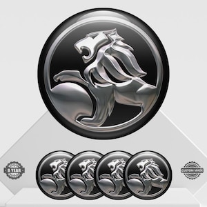 May include: A set of five chrome and black car emblems featuring a lion design. The emblems are circular with a silver lion in the center. The image includes a large emblem and four smaller ones, with warranty and custom-made badges.
