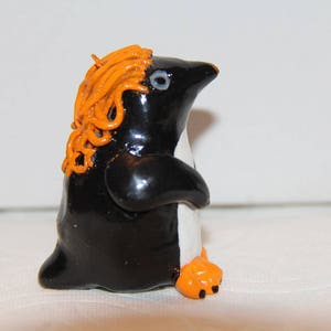 Peut inclure: Figurine de pingouin artisanal avec un corps noir, un ventre blanc et des pieds orange. Le pingouin a des cheveux bouclés orange et un œil bleu clair. Cette sculpture fantaisiste est un objet décoratif unique.