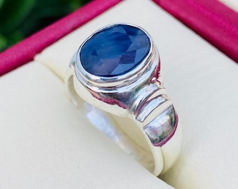 May include: A silver ring featuring a large, oval-cut, dark blue gemstone. The ring has a polished finish with a detailed band design. The gemstone is set in a bezel setting, showcasing its facets.