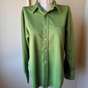 May include: A long-sleeved, button-down shirt in a vibrant green hue. The shirt features a classic collar, a chest pocket, and buttoned cuffs. The fabric has a subtle sheen, and the shirt is displayed on a mannequin.
