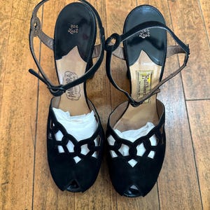May include: A pair of black high-heeled sandals with an open-toe design and a cutout lattice pattern on the vamp. The shoes feature an adjustable ankle strap with a buckle, a black insole with the text 324 Last, and brand labels.