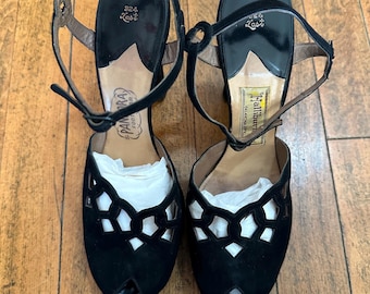 May include: A pair of black high-heeled sandals with an open-toe design and a cutout lattice pattern on the vamp. The shoes feature an adjustable ankle strap with a buckle, a black insole with the text 324 Last, and brand labels.