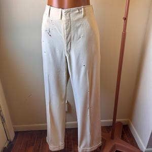 May include: Cream-coloured trousers with a straight leg and a cuffed hem. The trousers have several dark spots and are displayed on a mannequin. The trousers are a vintage style.