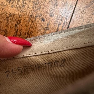 May include: The interior of a shoe featuring a light beige fabric lining with a visible stamped serial number reading 265899 552. The shoe has a cream-coloured leather trim along the top edge with visible stitching detail along the collar.