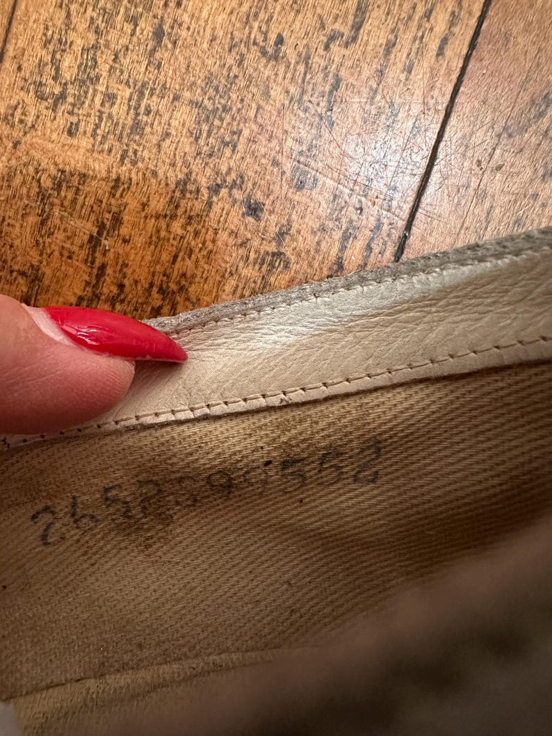 May include: The interior of a shoe featuring a light beige fabric lining with a visible stamped serial number reading 265899 552. The shoe has a cream-coloured leather trim along the top edge with visible stitching detail along the collar.
