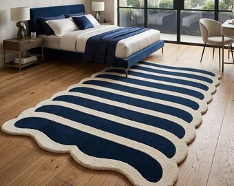 Pode incluir: Um tapete grande com design de bordas recortadas e listras alternadas em azul-marinho e creme. O tapete possui uma textura macia e um formato orgânico arredondado que cobre parte do piso de madeira em tom claro.