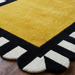 May include: A rectangular area rug featuring a large mustard yellow center panel surrounded by a thick black border. The border is decorated with a repeating pattern of white rectangular shapes along the scalloped edges of the rug.