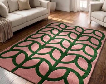 Può includere: Un tappeto rettangolare caratterizzato da una base color rosa tenue con un motivo geometrico ripetitivo verde scuro, composto da forme arrotondate e interconnesse simili a foglie che coprono l'intera superficie in una griglia simmetrica.