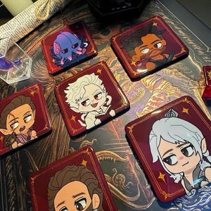 May include: Several square pins with red borders, each displaying a cartoon character illustration. The characters have distinct features and are set against a dark backdrop. The pins are arranged on a patterned surface, creating a visually appealing arrangement.