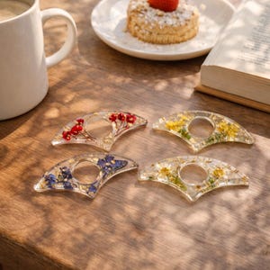 May include: Four clear resin thumb page holders, each with a different floral arrangement. One has red flowers, another yellow, a third blue, and the last has white and yellow flowers. Gold flakes are also embedded in the resin.
