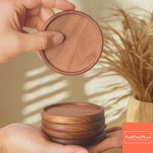 Puede incluir: Un conjunto de posavasos redondos de madera en tonos marrones. Un posavasos se sostiene sobre la pila, mostrando la veta natural de la madera. Los posavasos están diseñados para proteger las superficies.