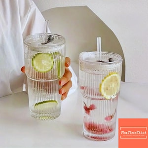Puede incluir: Dos vasos de vidrio transparente y acanalado con tapas y pajitas. Uno contiene una rodaja de limón, el otro flores rosas. Los vasos están llenos de líquido. La imagen incluye el texto "TeaTimeThish".