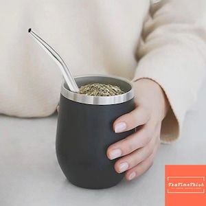 Peut inclure: Une calebasse à maté noire à double paroi avec un bord argenté et une paille en acier inoxydable. La calebasse est remplie d'herbes séchées. L'image comprend le logo TeaTimeThish en bas à droite.