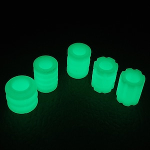 Puede incluir: Cinco objetos cilíndricos verdes brillantes, con diferentes texturas y formas, sobre un fondo negro. Los objetos parecen estar hechos de un material translúcido, emitiendo una luz verde brillante. Los objetos miden aproximadamente 2 cm de altura.