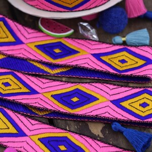 May include: A roll and strips of woven fabric trim featuring a repeating geometric diamond pattern in vibrant shades of hot pink, royal blue, and golden yellow, with thin black embroidered outlines defining each shape throughout the design.