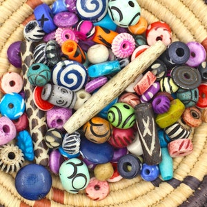May include: A woven basket filled with colorful beads in various shapes and sizes, including round, cylindrical, and oval beads. The beads are made of wood, bone, and plastic.