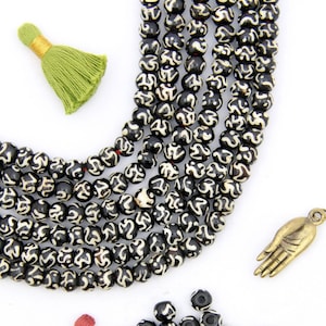 May include: Black and white bone beads with a swirling pattern, a small pile of loose beads, and two tassels. The beads are strung on a cord and are used for making jewelry.