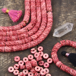 以下が含まれることがあります： ピンク色の彫刻ビーズとビーズストランドのコレクション。ビーズは赤みがかったピンク色で、彫刻された幾何学模様です。ピンクのタッセルと透明なクリスタルも存在します。