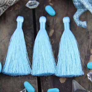 May include: Three light blue tassels with a fluffy texture. The tassels are arranged in a row on a wooden surface.