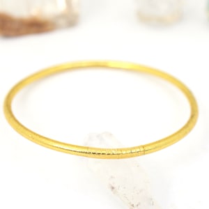 May include: A simple gold bangle bracelet with a textured surface.