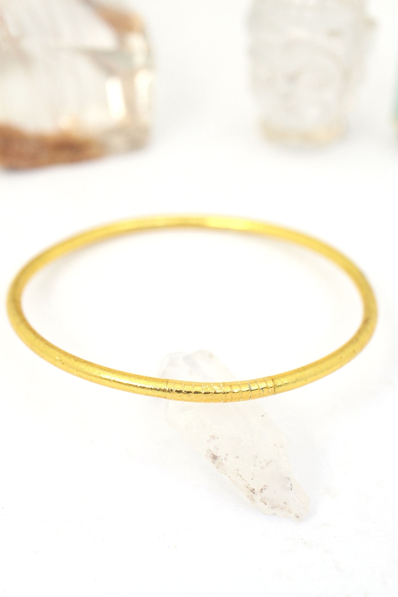 May include: A simple gold bangle bracelet with a textured surface.