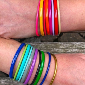 May include: A stack of colorful bangle bracelets in shades of yellow, orange, red, pink, purple, and green. The bracelets are stacked on a person's wrist.