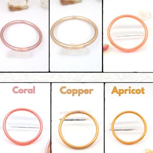 May include: Six colorful bangles in rose gold, champagne, ginger, coral, copper, and apricot. Each bangle is a simple, round design. The names of the colors are written above each bangle.