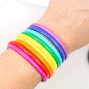 May include: A stack of colorful bracelets in a rainbow pattern. The bracelets are made of a smooth, glossy material and are worn on a person's wrist.