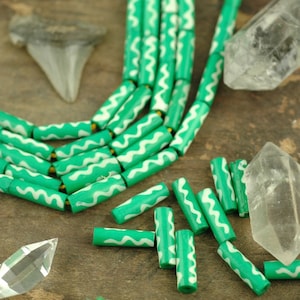May include: A strand of green and white patterned beads, with additional beads scattered around. The beads are made of wood and have a wavy design.