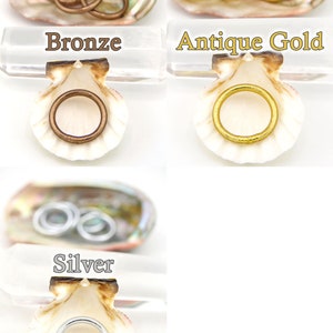 May include: Three sets of jump rings in different finishes: bronze, antique gold, and silver. Each set is displayed in a seashell.