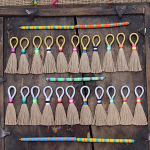 May include: A collection of colorful tassel keychains with gold and silver rings. The tassels are made of natural fibers and are arranged in two rows on a wooden surface.