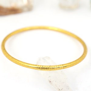 May include: A gold bangle bracelet with a textured surface.