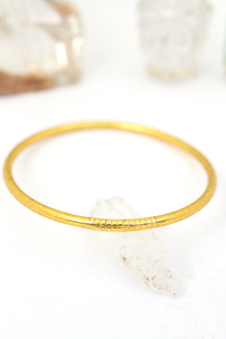 May include: A gold bangle bracelet with a textured surface.
