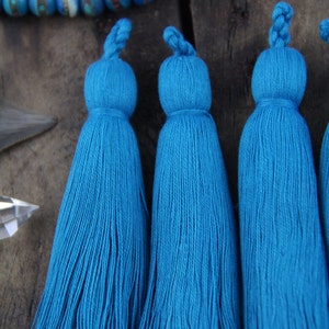 May include: Four teal blue tassel ornaments with a knotted top. The tassels are made of soft, fluffy yarn and are approximately 4 inches long.
