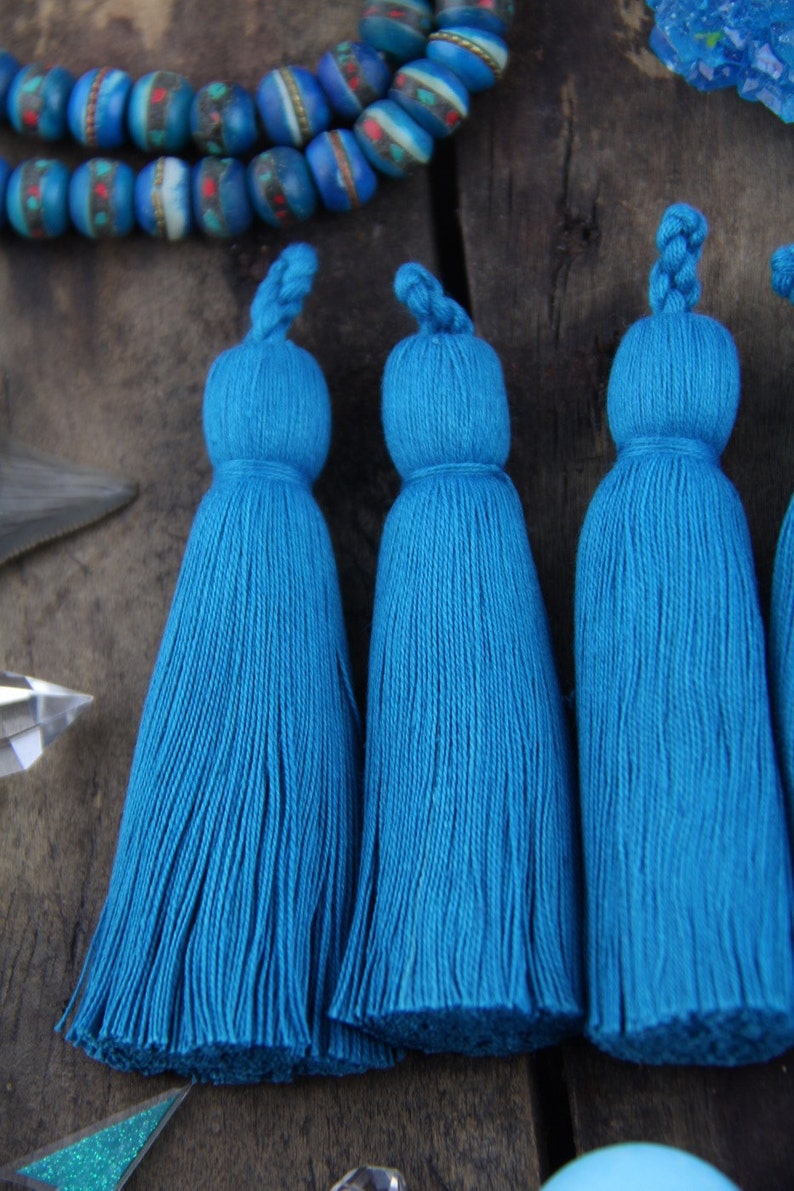 May include: Four teal blue tassel ornaments with a knotted top. The tassels are made of soft, fluffy yarn and are approximately 4 inches long.