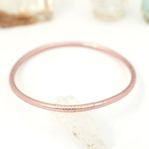 May include: A delicate rose gold bangle bracelet with a textured finish.