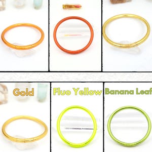 May include: A collection of colorful, thin, circular rings in various shades, including orange, light gold, gold, and fluo yellow. Each ring is displayed against a white background, with the color name labeled above each ring.