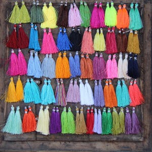 May include: A collection of colorful tassels in various shades of blue, green, red, orange, yellow, pink, purple, and white. The tassels are arranged in rows in a wooden box.