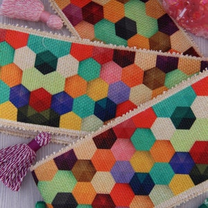 May include: Three colourful fabric ribbons with a geometric honeycomb pattern. The ribbons are made of a natural woven fabric with a white border. The honeycomb pattern is made up of various colours, including red, orange, yellow, green, blue, purple, and brown.