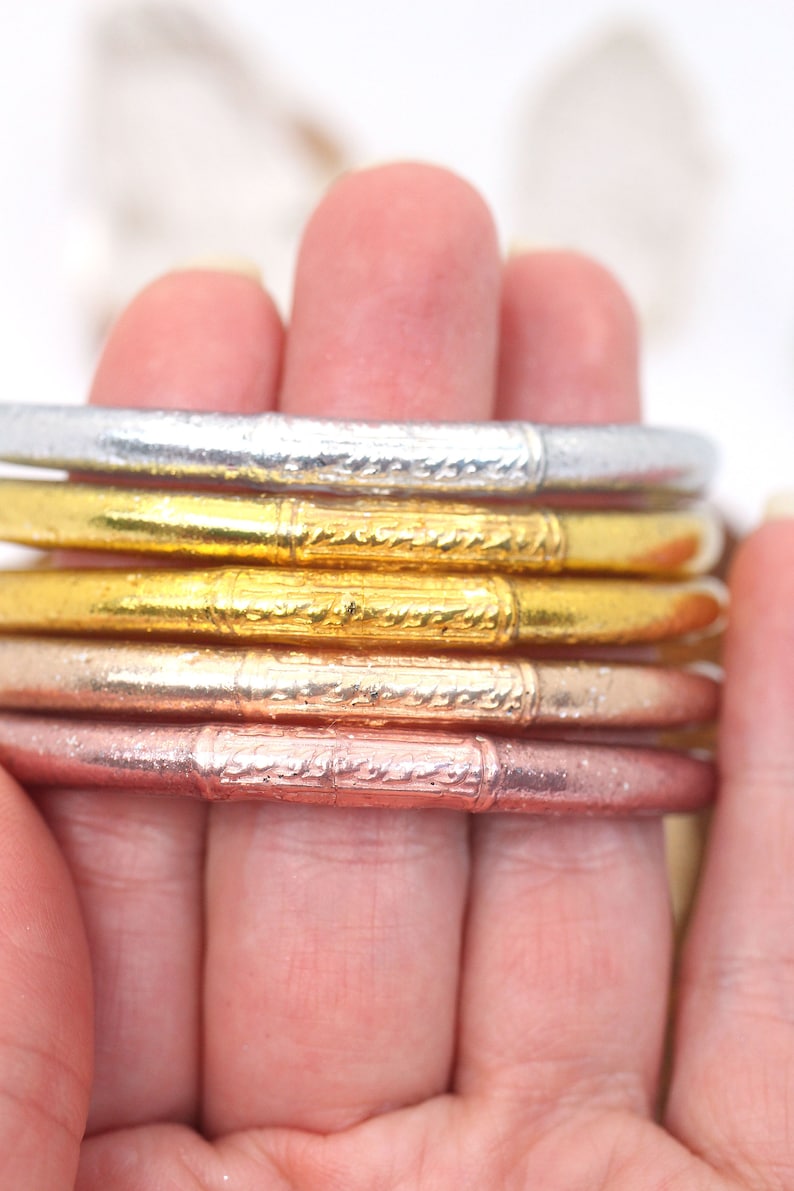 May include: A stack of four silver, gold, and rose gold bangles with an intricate etched design.
