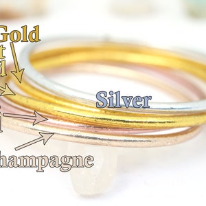 May include: Four stacked rings in different colors: champagne, rose gold, light gold, and silver.