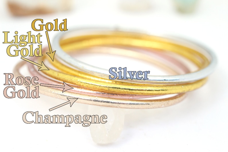 May include: Four stacked rings in different colors: champagne, rose gold, light gold, and silver.