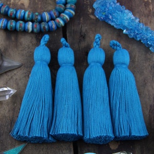 May include: Four teal blue tassels with a long fringe. The tassels are made of a soft, fluffy material and are perfect for adding a touch of bohemian style to any project.