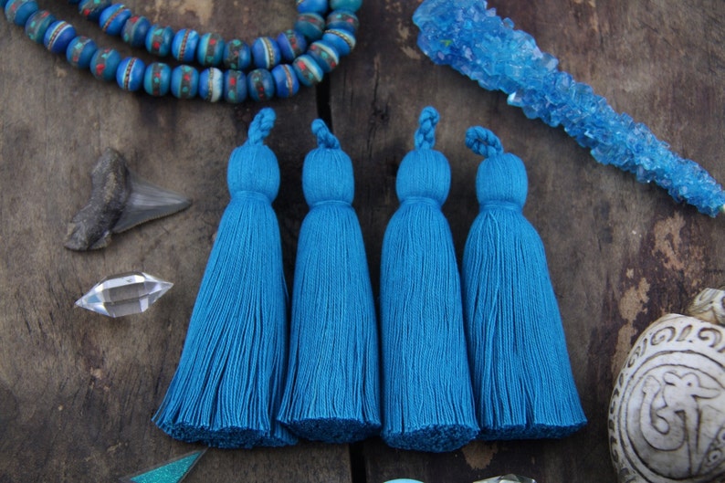 May include: Four teal blue tassels with a long fringe. The tassels are made of a soft, fluffy material and are perfect for adding a touch of bohemian style to any project.