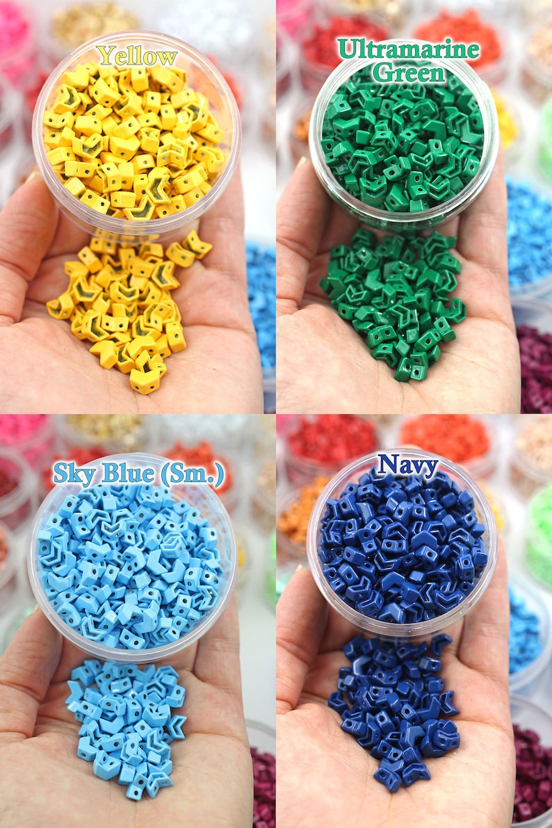K&ouml;nnte beinhalten: Vier Beh&auml;lter mit kleinen, pfeilf&ouml;rmigen Plastikperlen in verschiedenen Farben: Gelb, Gr&uuml;n, Hellblau und Marineblau. Die Perlen befinden sich in durchsichtigen Beh&auml;ltern und fallen auf eine Hand.