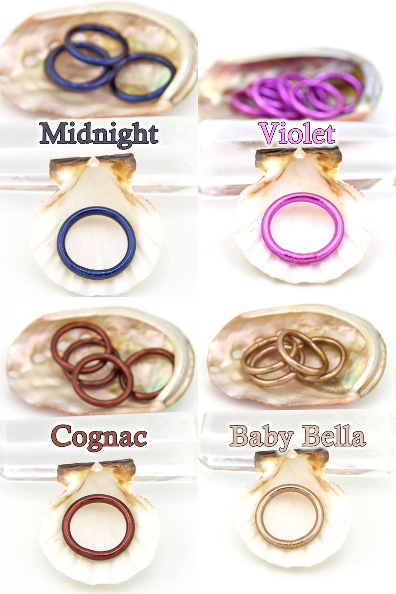 May include: Four sets of colorful metal rings in different colors, including midnight blue, violet, cognac, and baby bella, displayed in seashells. The rings are arranged in a single row, with each set in its own seashell.
