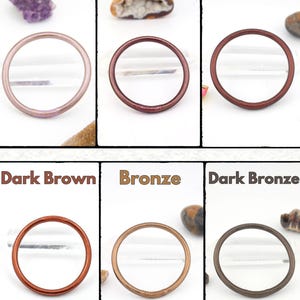 May include: Six circular hair ties in various colors: Portobella, Mocha, Cognac, Dark Brown, Bronze, and Dark Bronze. Each tie is displayed against a white background with a small decorative stone.