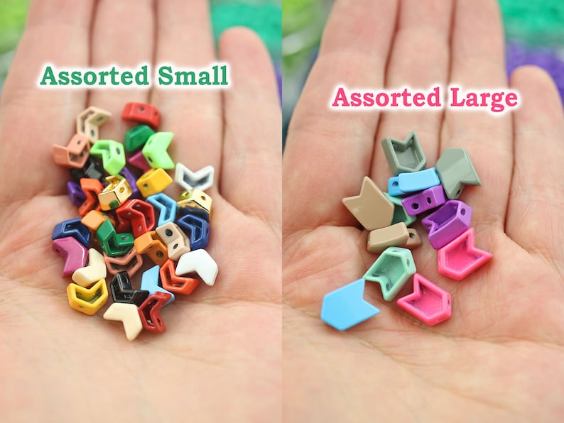 K&ouml;nnte beinhalten: Sortiertes kleine und gro&szlig;e pfeilf&ouml;rmige Metallperlen in verschiedenen Farben. Die Perlen sind in zwei Haufen auf der Hand einer Person angeordnet. Der Text "Assorted Small" befindet sich &uuml;ber den kleineren Perlen und der Text "Assorted Large" &uuml;ber den gr&ouml;&szlig;eren Perlen.